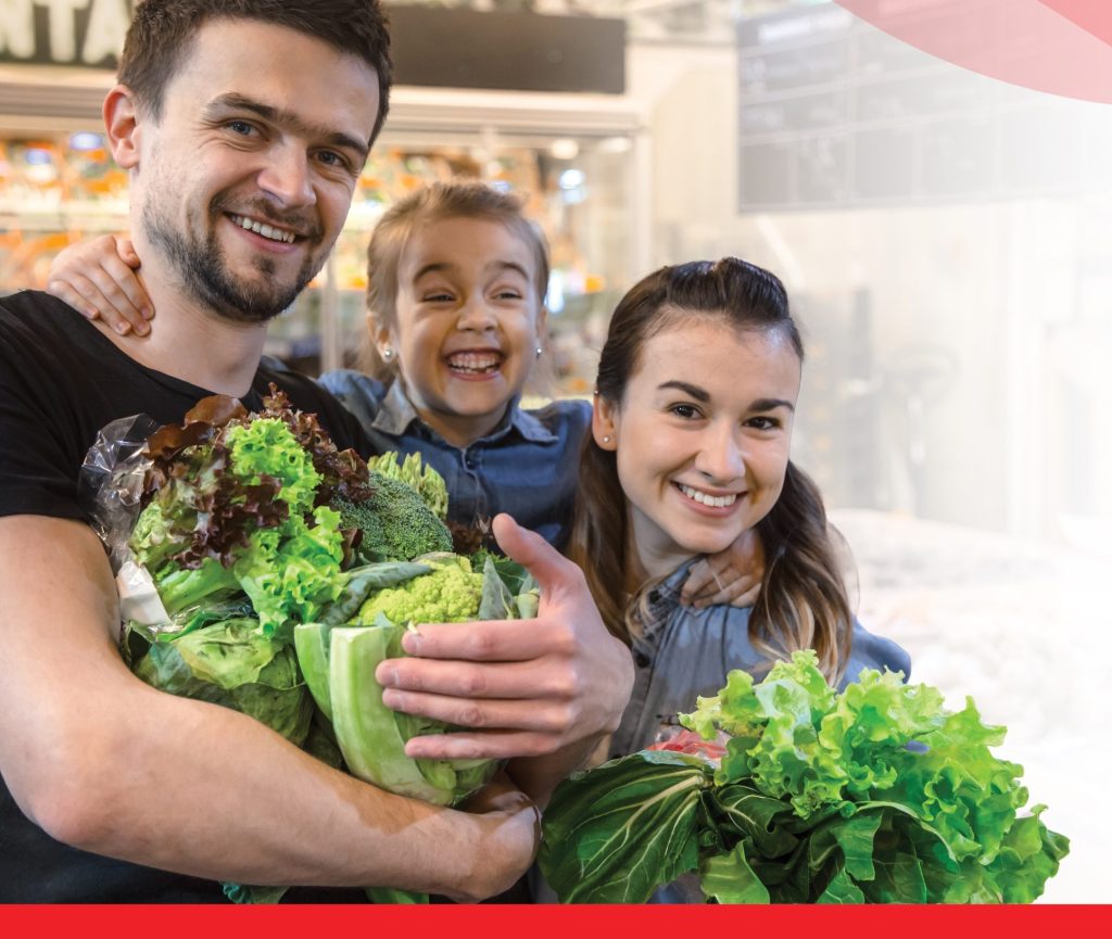 Smiling family holding leafy greens in a grocery store.