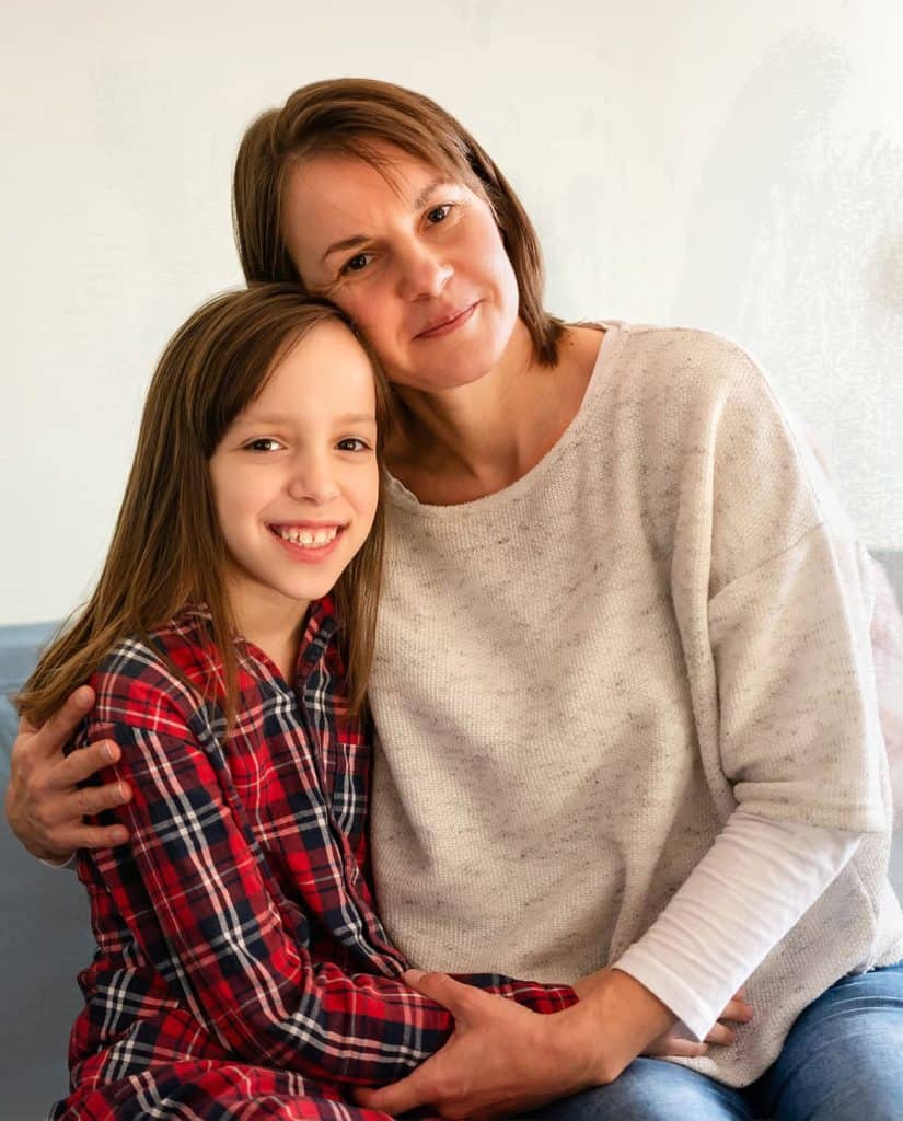 A woman hugs a smiling young girl.